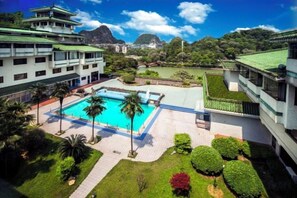 A swimming pool surrounded by manicured lawns and a building with a traditional architectural style. - Guilin Park Hotel (GUILIN)