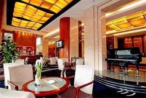 A lobby with a grand piano, comfortable seating, a glass table, and a television screen. - Metropolitan Hotel (DONGGUAN)