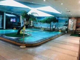 Piscina interna com tema tropical, incluindo palmeiras e um mural com cachoeira.