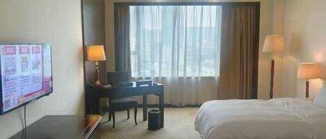 A hotel room with two beds, a desk with a chair, a television, and a large window with curtains.