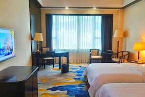Quarto de hotel com duas camas, uma escrivaninha, uma cadeira e televisão na parede.