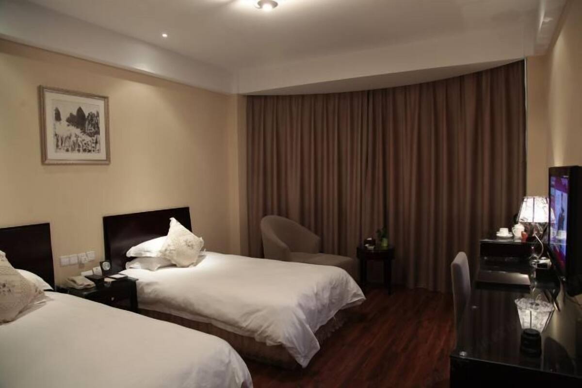 Ein Hotelzimmer mit zwei Betten, einem Schreibtisch, einem Stuhl, einem Fernseher und einem Vorhang.
