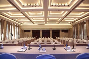 Un salón de conferencias con hileras de sillas, un escenario y micrófonos.
