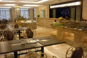 Une salle à manger d’hôtel avec des tables, des chaises, un buffet et une grande fenêtre.