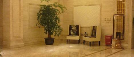 A lobby with a potted plant, two armchairs, and a framed artwork on the wall.