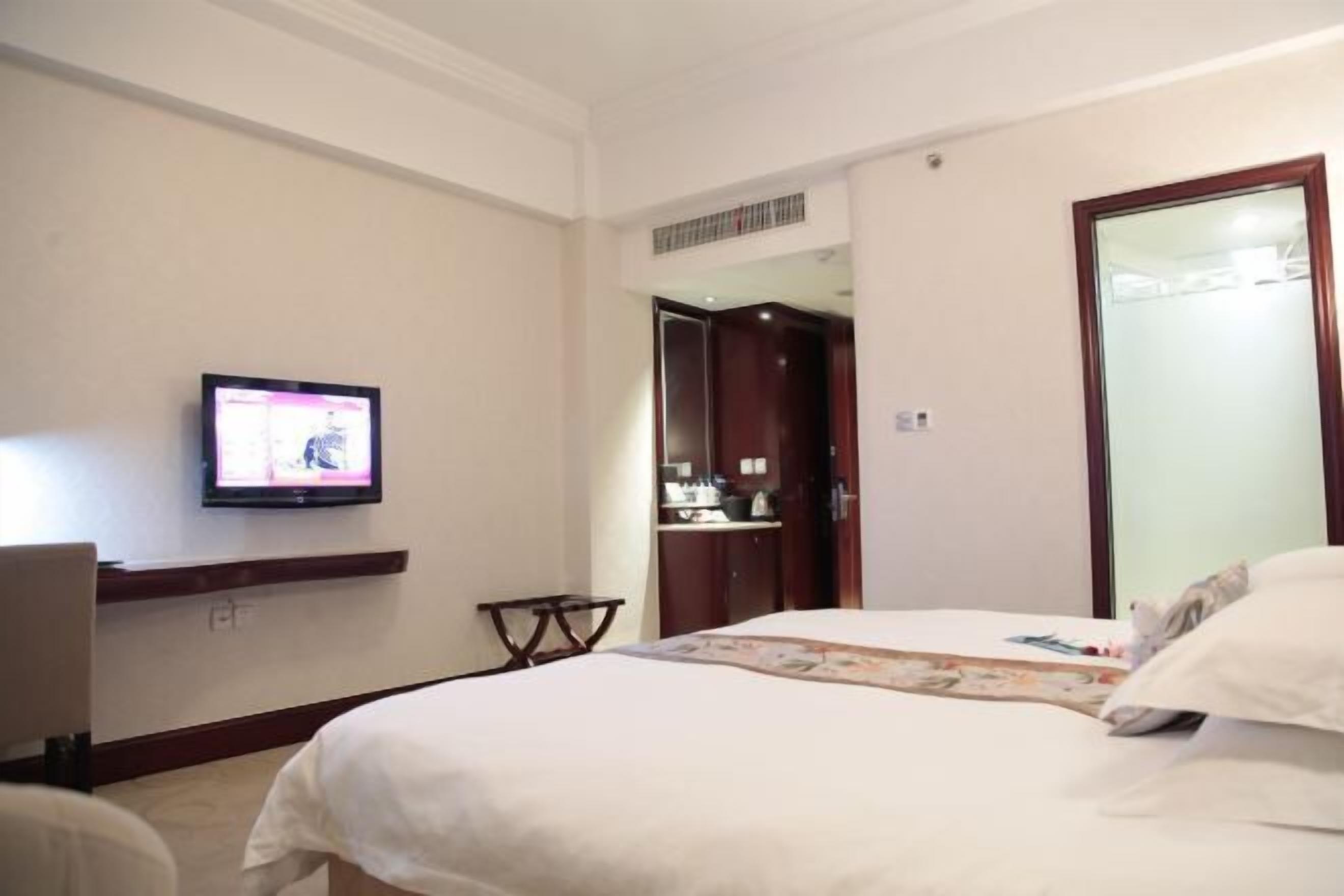 A hotel room with a bed, a television mounted on the wall, a desk, and a wardrobe.
