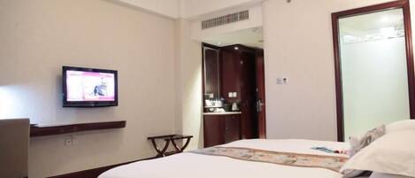 Una habitación de hotel con cama, televisor montado en la pared, escritorio y armario.