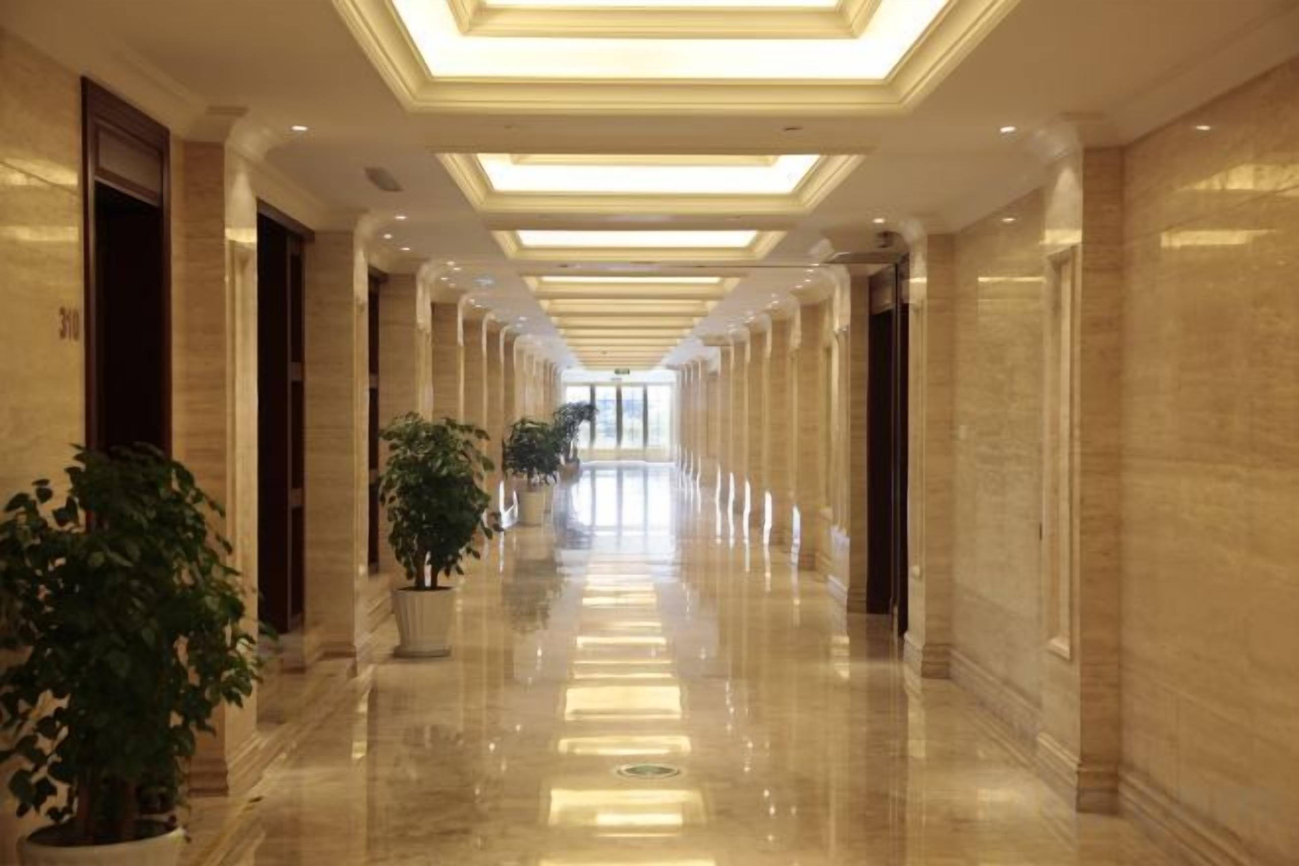 A long, well-lit hallway with marble floors and potted plants.