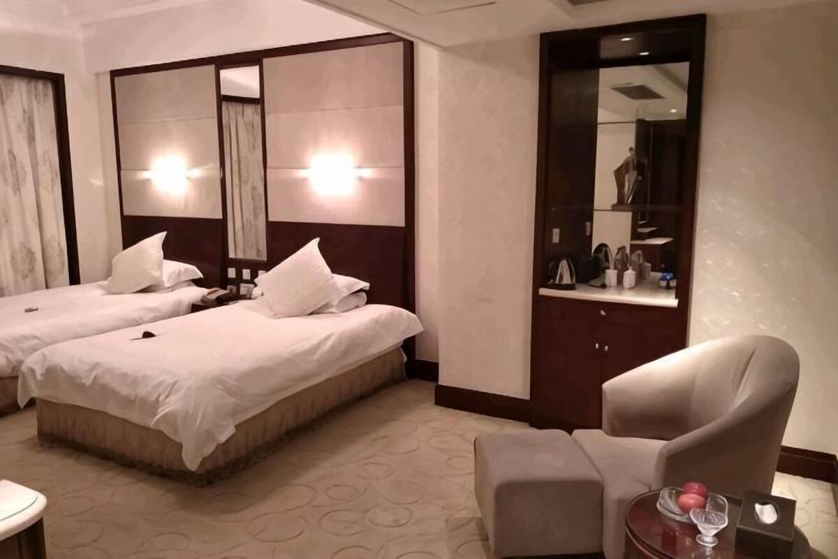 Ein Hotelzimmer mit zwei Betten, einem Sessel, einem kleinen Tisch und einem Spiegel.