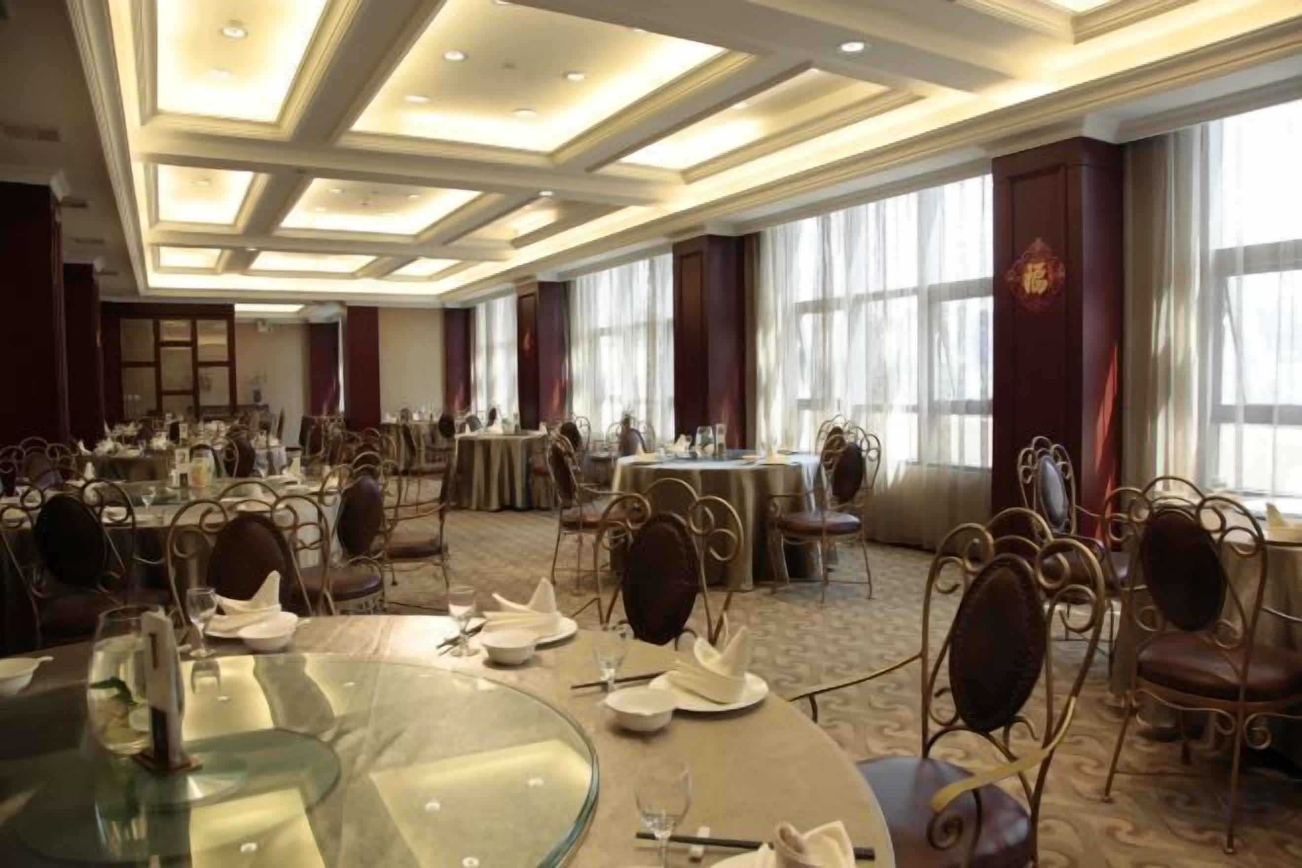 Salão de banquetes com mesas redondas, cadeiras e piso coberto por carpete.