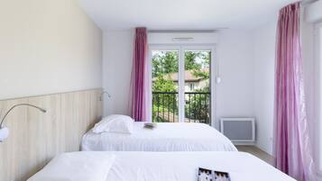 Een hotelkamer met twee bedden, een raam met roze gordijnen, een plafondlamp en uitzicht op groen.