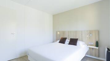 Habitación de hotel moderna con una cama grande, cabecera de madera, lámparas de noche, un estante pequeño con una botella de agua y un enchufe.
