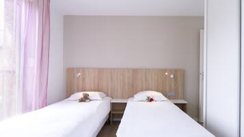 A hotel room with two single beds, a wooden headboard, a nightstand, and a window with pink curtains.