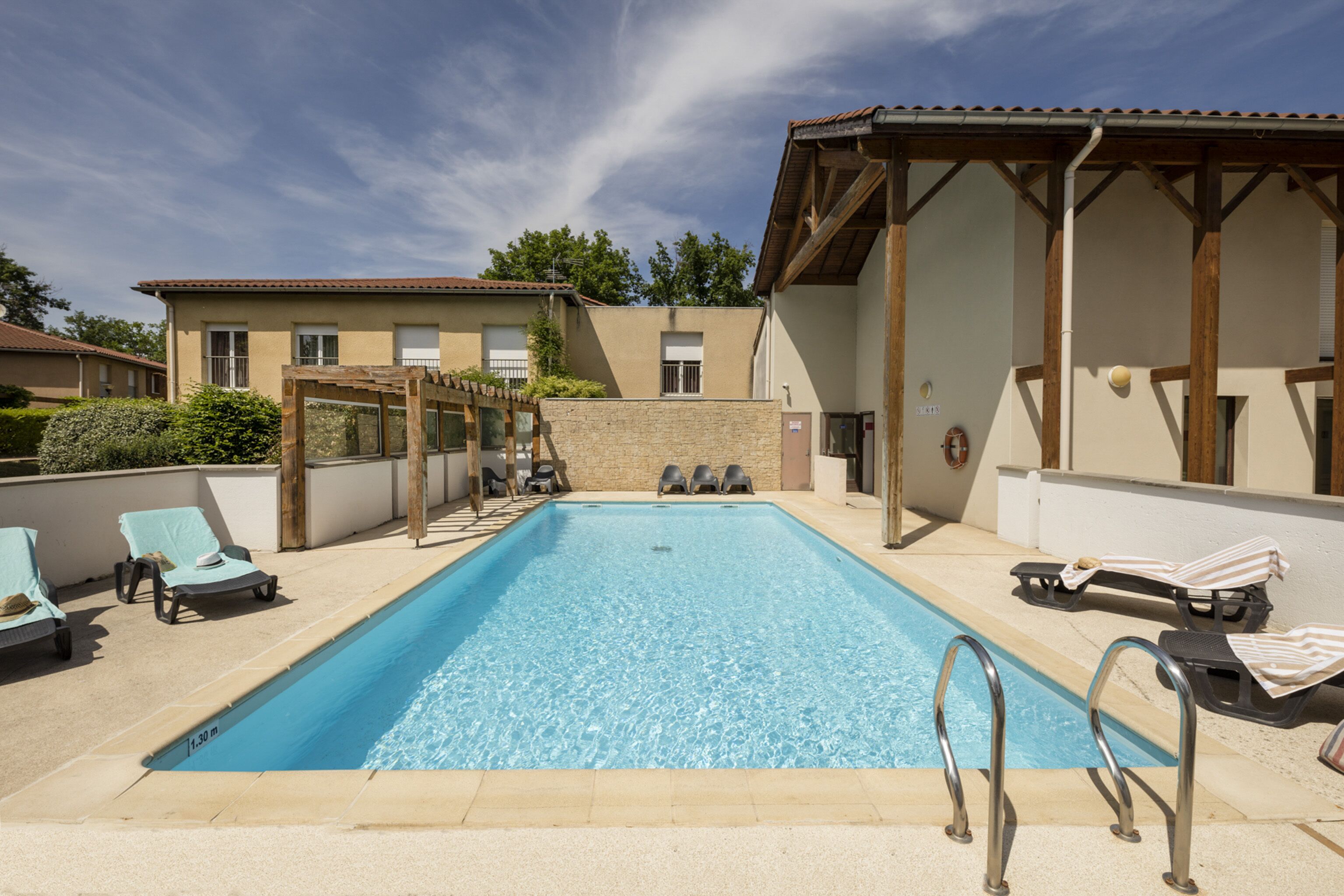 A rectangular swimming pool with clear blue water, surrounded by lounge chairs and a pergola.