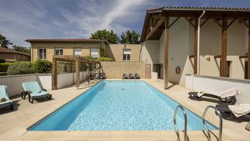 A rectangular swimming pool with clear blue water, surrounded by lounge chairs and a pergola.