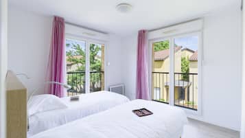 A hotel room with two beds, a desk, and a window with a view of a balcony and buildings.