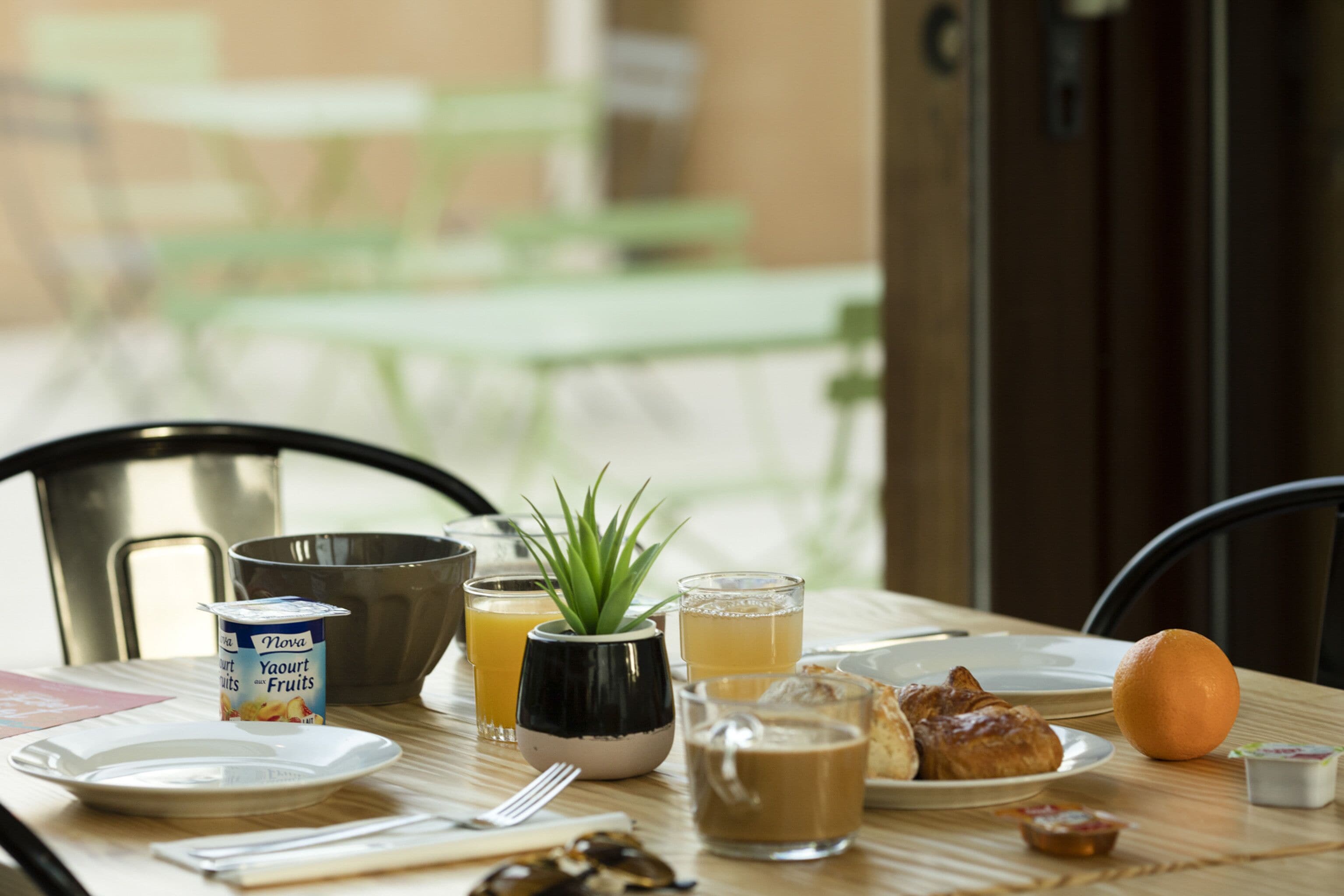 Een ontbijttafel met een kom, een bloempot, een glas sinaasappelsap, een kop koffie, en een bord met eten.