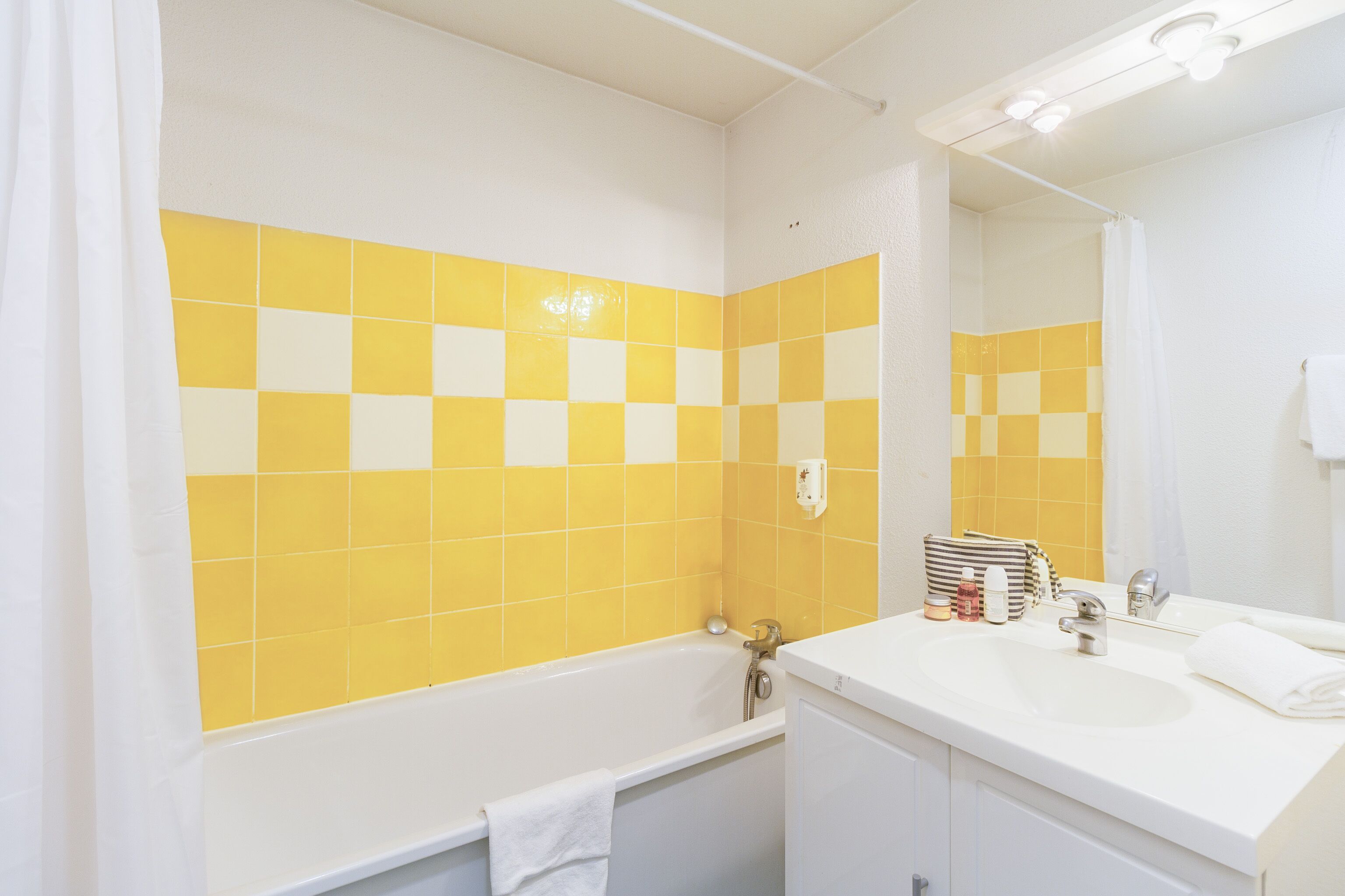 Un baño con un lavamanos blanco, un espejo y paredes con azulejos amarillos.