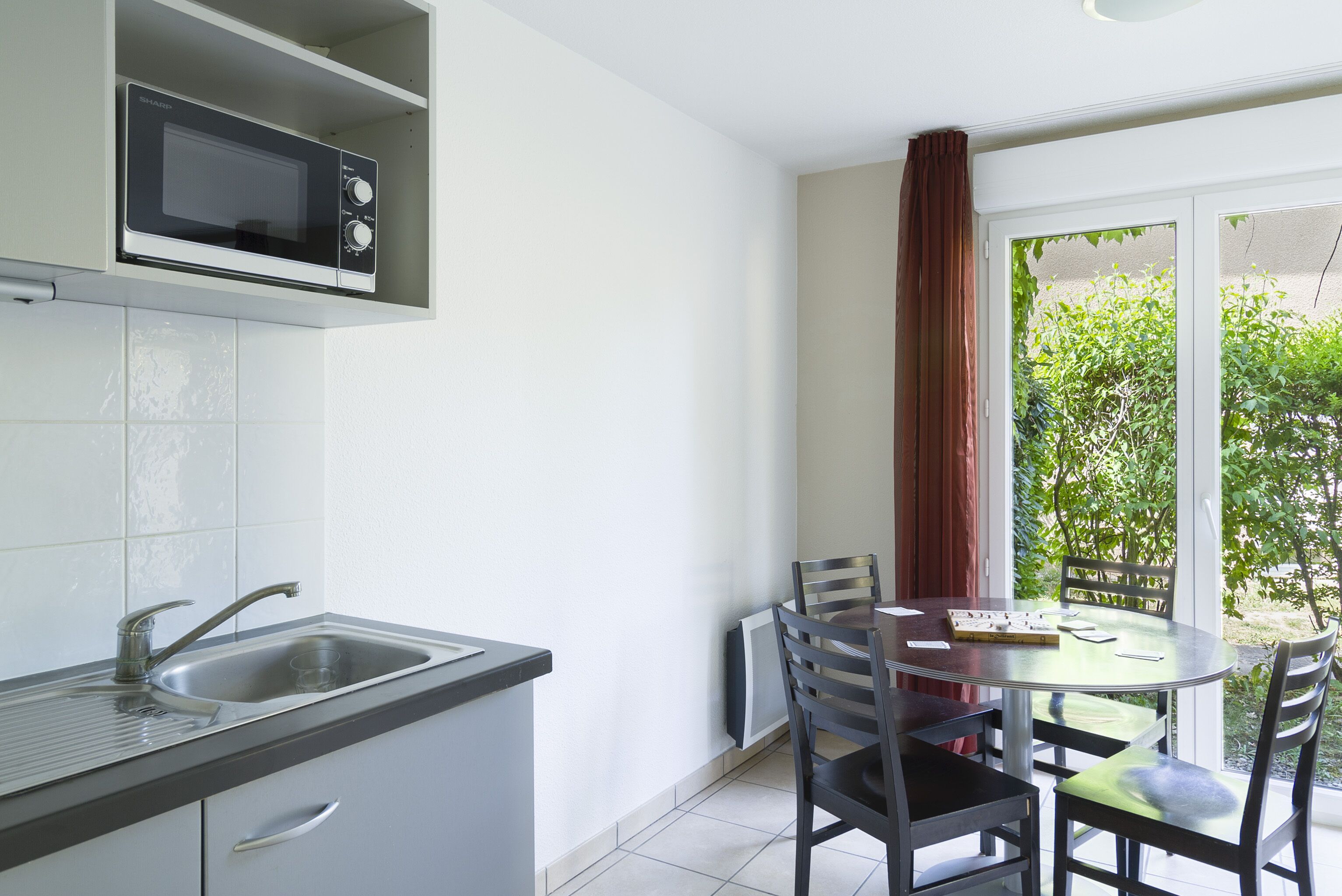 Cocina compacta con microondas integrado, un lavabo y una zona de comedor con mesa y sillas.