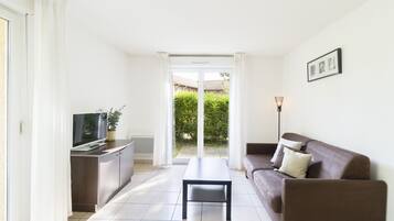 A modern living room with a sofa, a coffee table, and a TV on a cabinet. There is a sliding glass door leading to a garden.