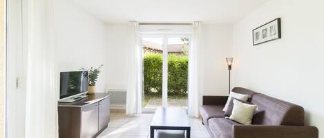Een moderne woonkamer met een bank, een salontafel en een televisie op een kast. Er is een schuifdeur naar een tuin.