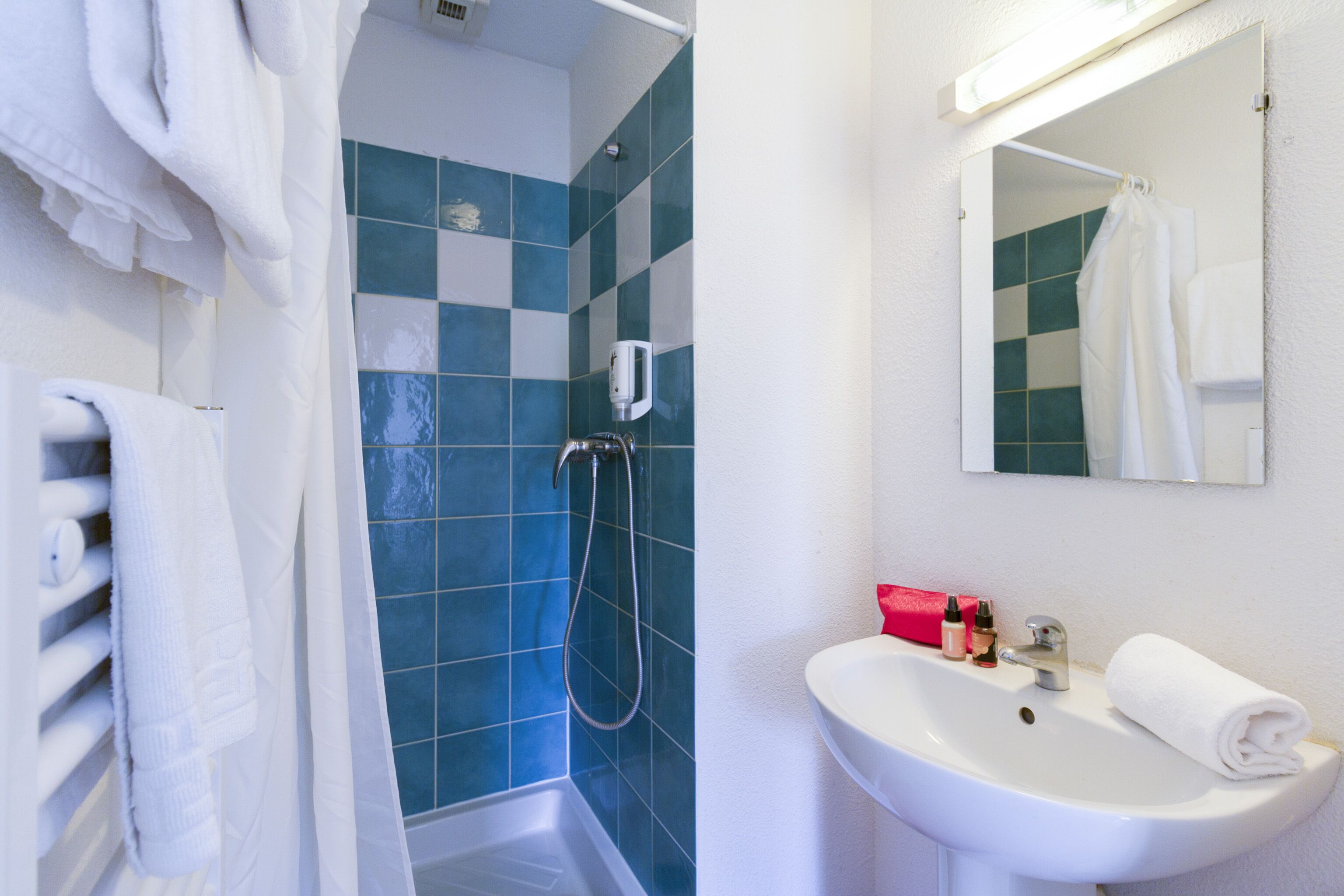 A bathroom with a white sink, blue tiles, a shower, and a mirror.