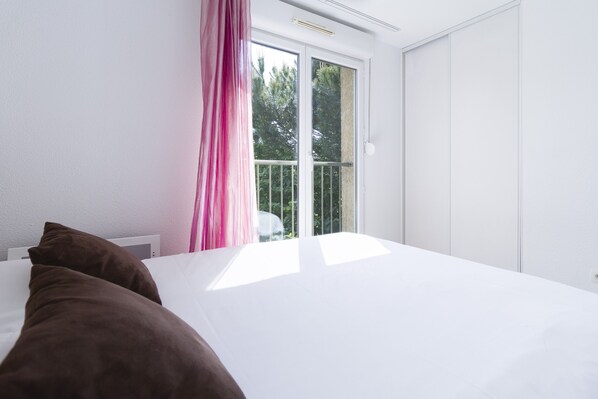 A bedroom with a large bed, a window with a view of trees, and a white door.