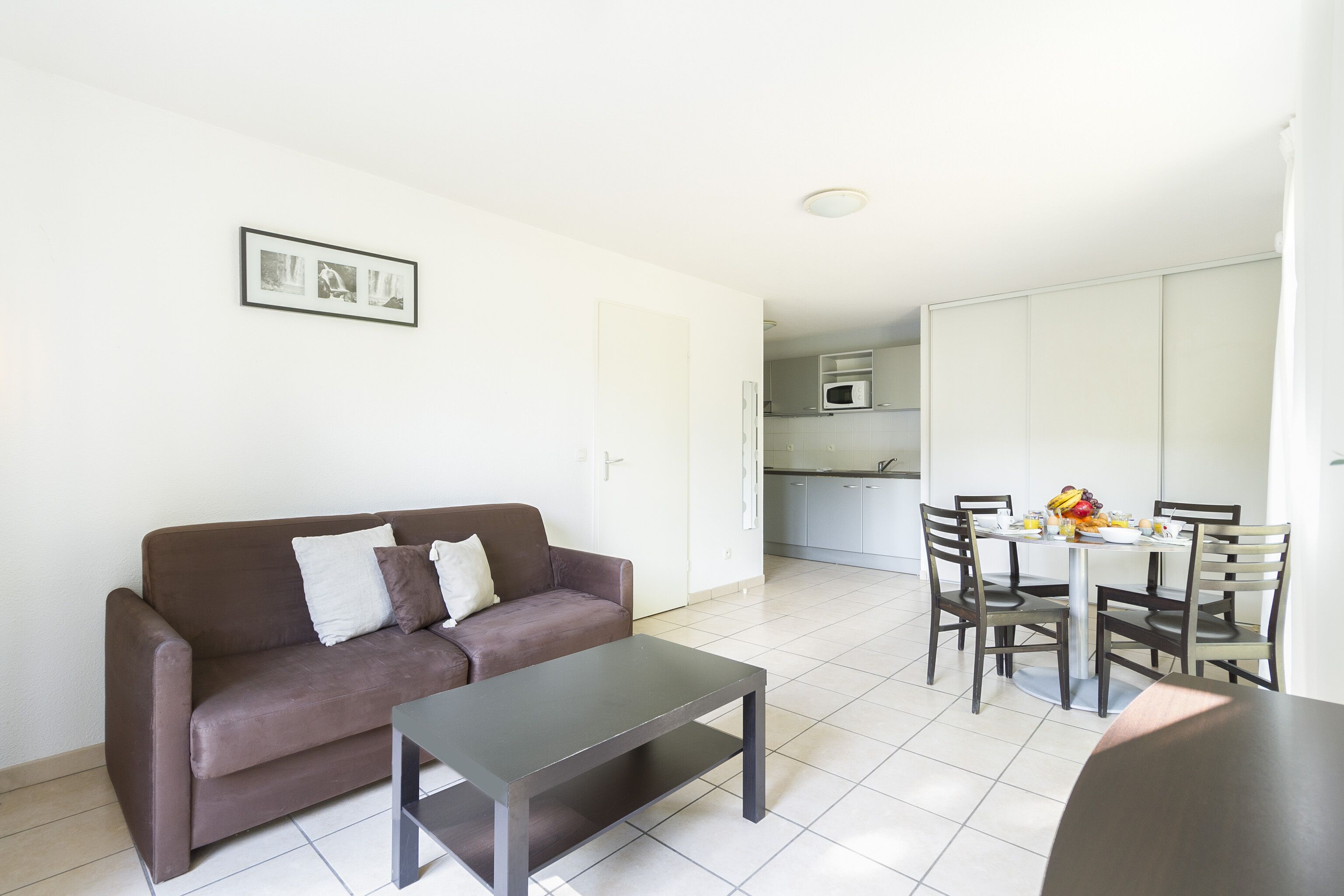 Un salon moderne avec un canapé marron, une petite table et un coin repas comprenant une table et des chaises blanches.