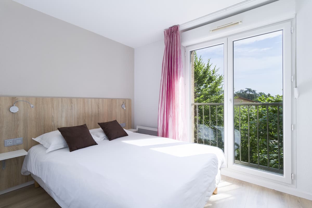 Une chambre à coucher avec un lit, une tête de lit en bois, une table de chevet et une fenêtre donnant sur un paysage verdoyant.