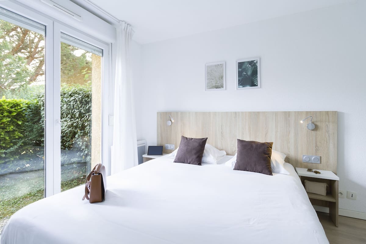 Une chambre d’hôtel moderne avec un grand lit, une table de chevet avec une lampe et une vue sur la verdure.