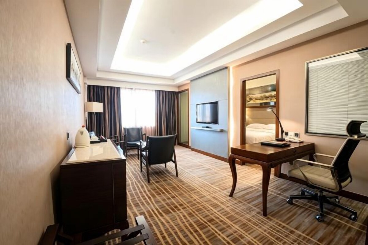 Une chambre d’hôtel équipée d’un lit, d’un bureau, d’une chaise, d’une télévision et d’une fenêtre avec des rideaux.