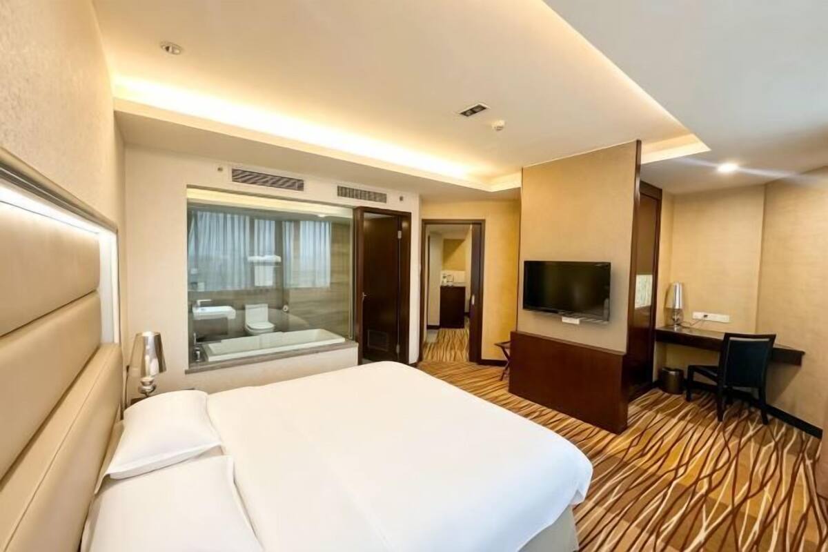 A hotel room with a bed, a desk, a television, and a bathroom with a mirror and shower.