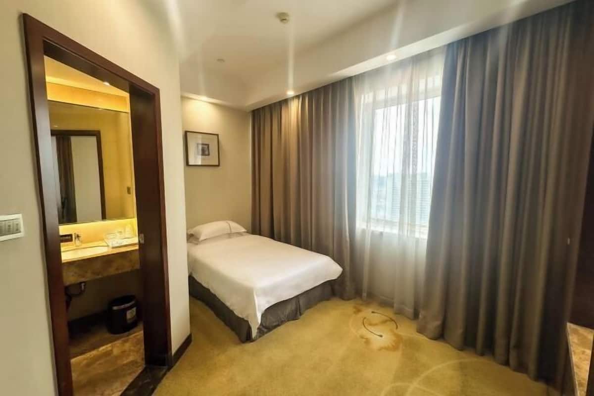 A hotel room with a bed, a bathroom with a mirror, and a window with curtains.