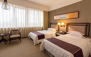 A hotel room with two beds, a chair, a small table, and a nightstand with a lamp.