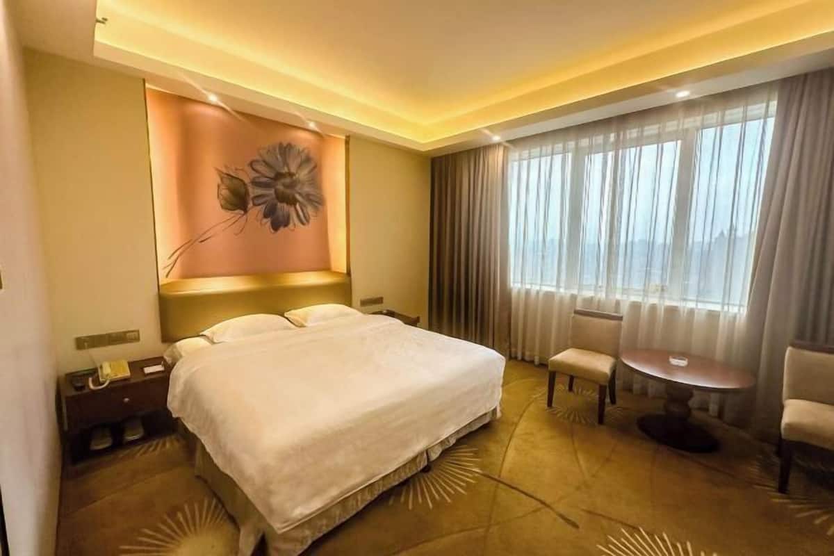 A hotel room with a large bed, a desk, a chair, a round table, and a window with curtains.