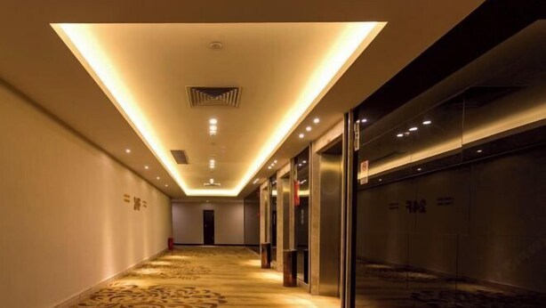 A hotel corridor with a patterned carpet, recessed lighting, and glass doors leading to elevators. - Celeste Palace Hotel (Jiangmen)