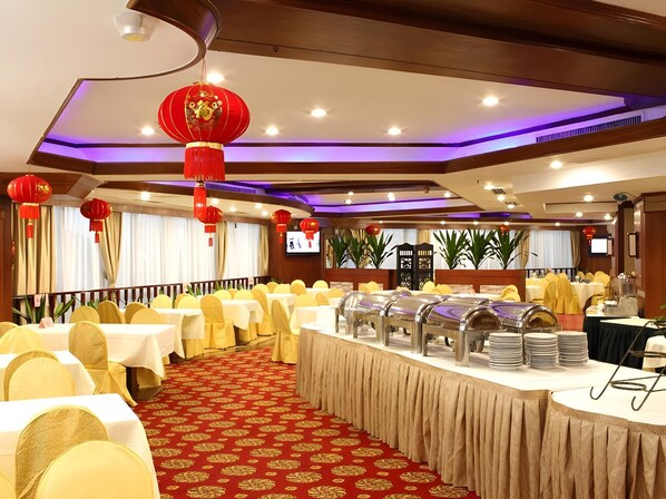 A banquet hall with round tables, yellow chairs, red lanterns, and a buffet setup.