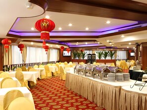 Une salle de banquet avec des tables rondes, des chaises jaunes, des lanternes rouges et un buffet.