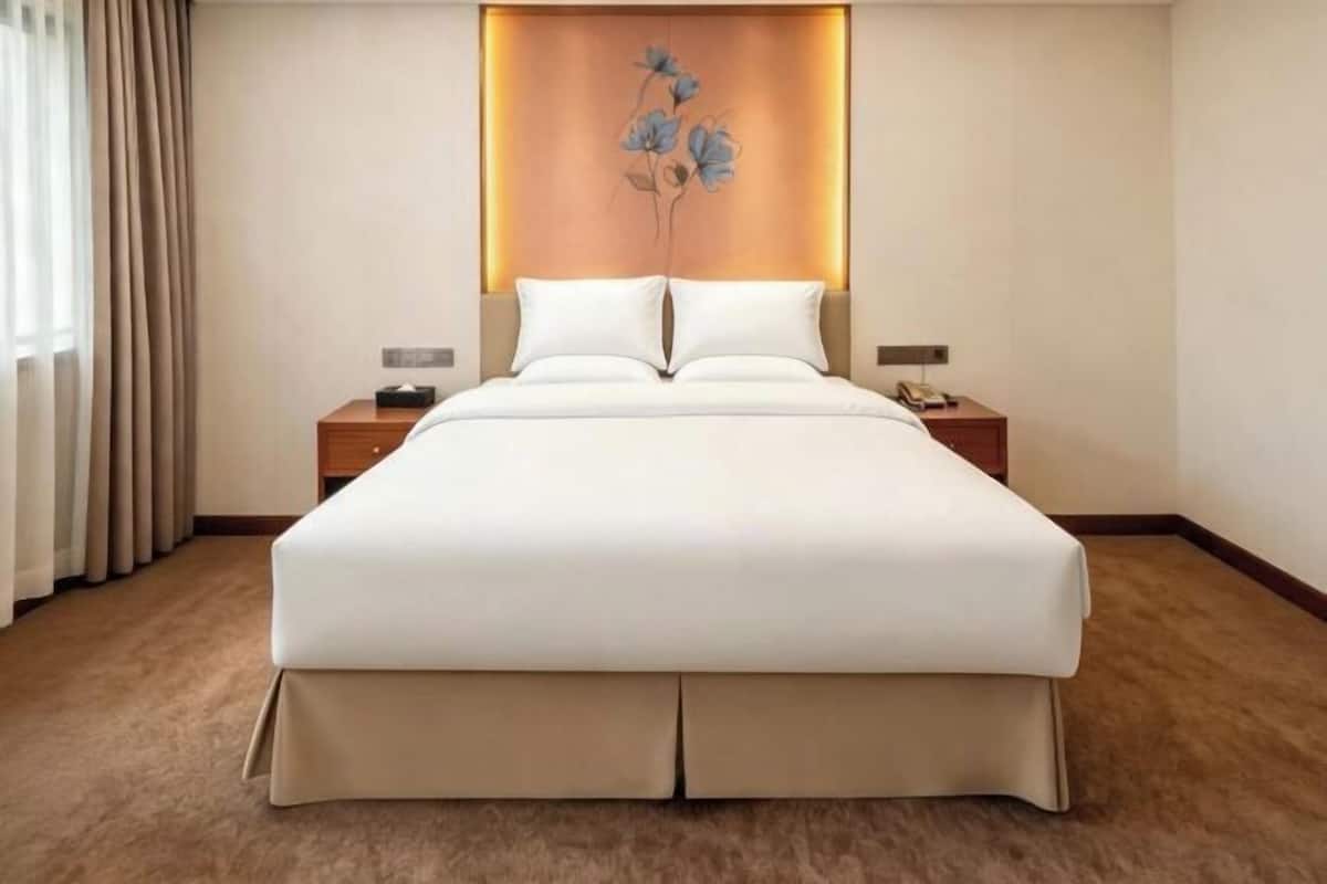 A hotel room with a large bed, two bedside tables, a headboard with a floral design, and a carpeted floor.