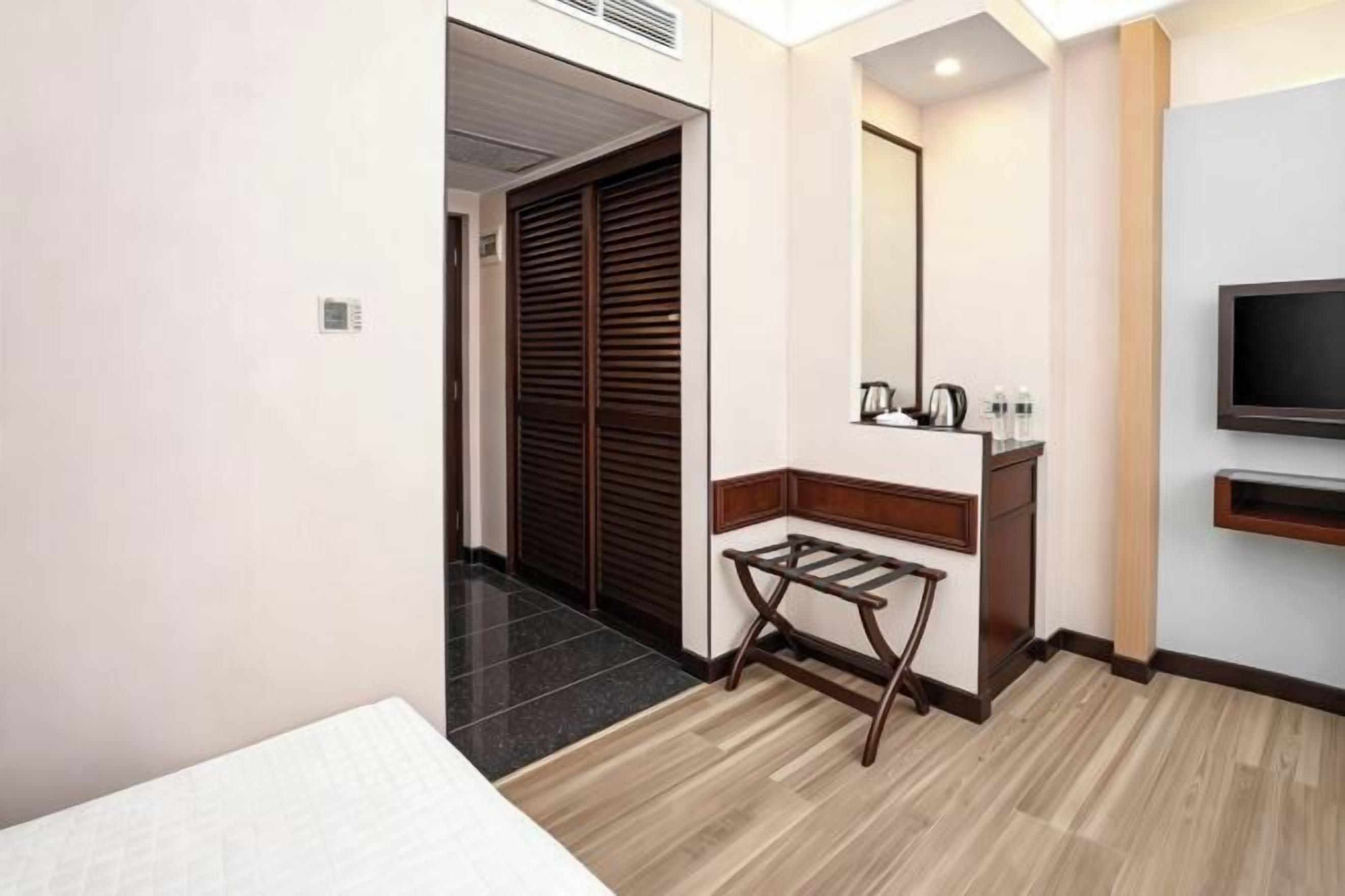 Une chambre d’hôtel avec un lit, un banc en bois, une télévision, un miroir et une porte donnant sur une autre pièce.