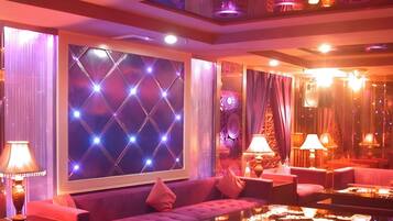 A room with a large window, a sofa, a table, and lamps.