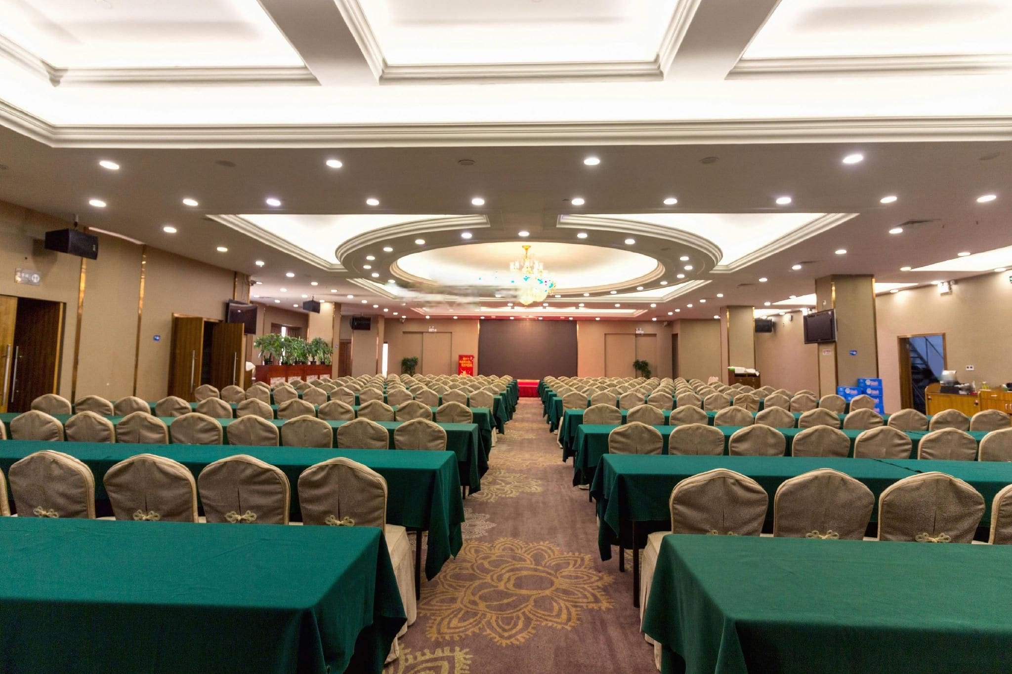 A conference room with rows of tables and chairs, a carpeted floor, and a chandelier.