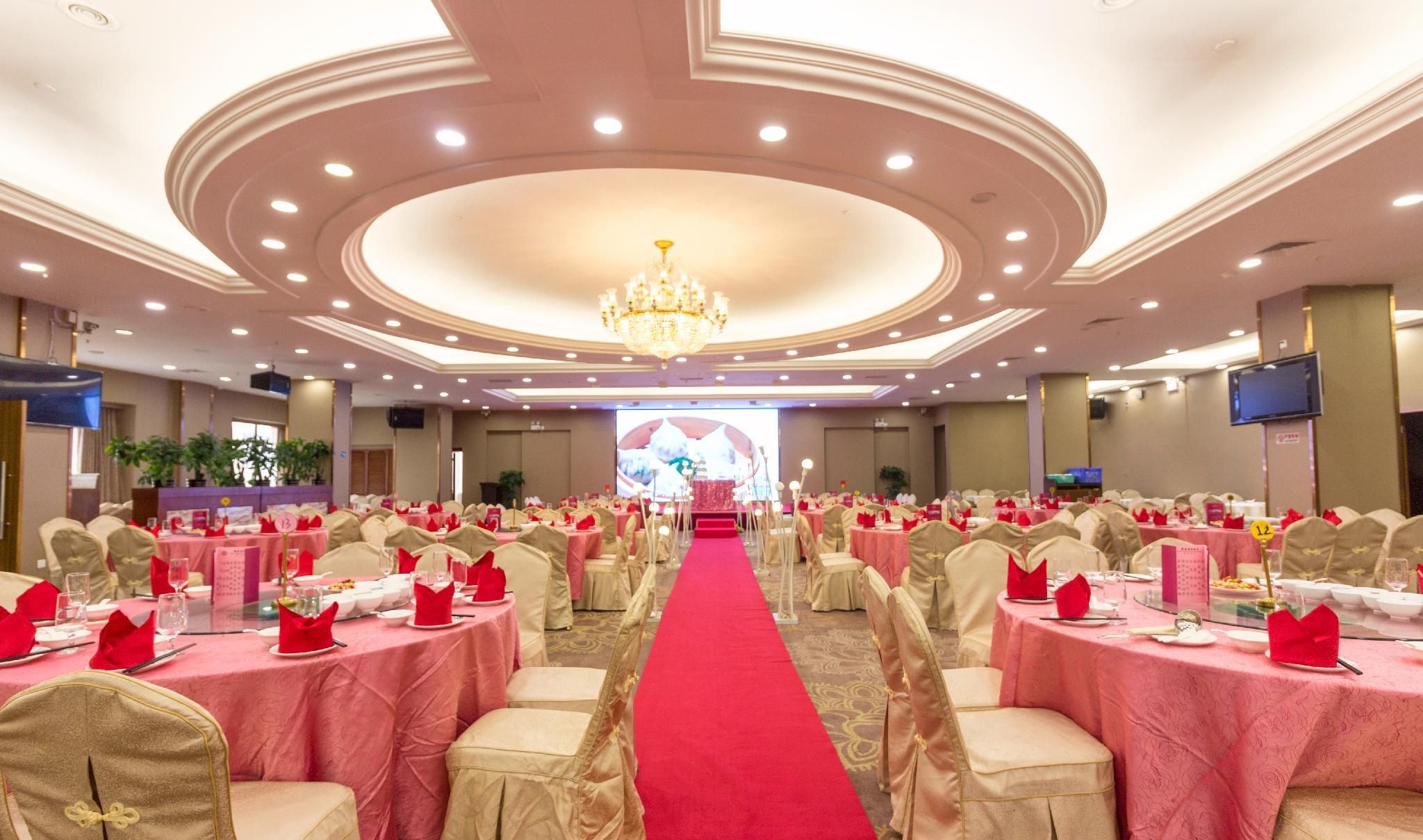 Une salle de banquet avec des tables rondes, une moquette rouge et un lustre.