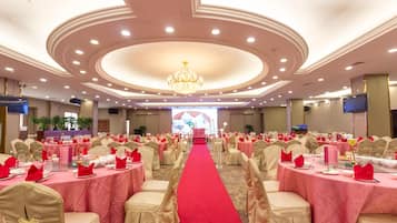Une salle de banquet avec des tables rondes, une moquette rouge et un lustre.