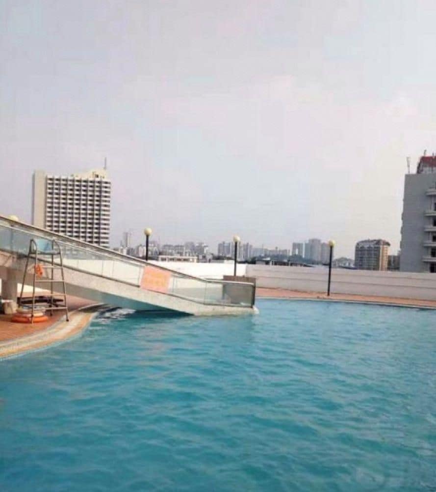 Une piscine avec un pont, des immeubles de la ville en arrière-plan et un ciel dégagé.