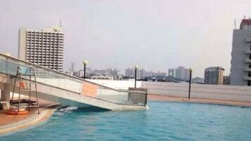 Une piscine avec un pont, des immeubles de la ville en arrière-plan et un ciel dégagé.