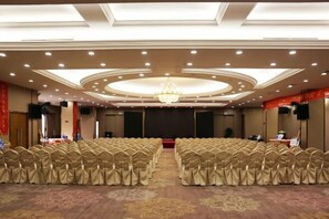 A conference room with rows of chairs, a stage, and a chandelier.