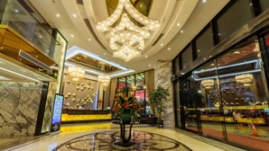 Un hall d’hôtel agrémenté d’un grand lustre, d’un comptoir d’accueil et d’une composition florale décorative.