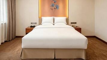 A hotel room with a large bed, two bedside tables, a nightstand, a wall-mounted telephone, and a decorative wall panel.