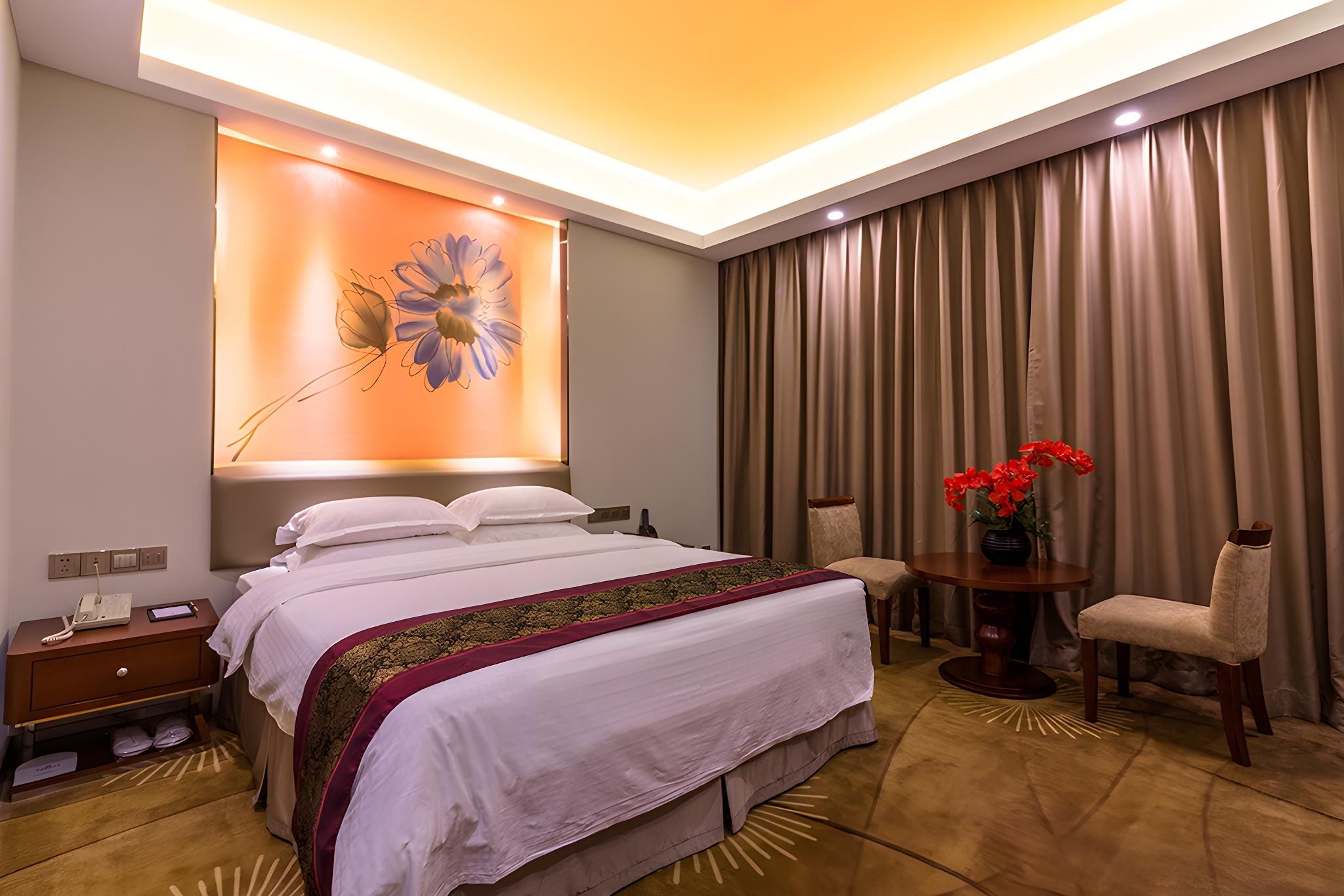 A hotel room with a bed, bedside table, lamp, chair, and a large window with curtains.